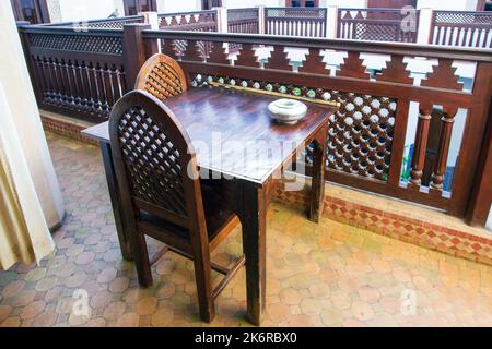 Alcuni tavoli e sedie in legno con decorazioni arabiche e ringhiere in legno e pareti figurate sotto di essi e un tavolo e una sedia, con una tipica sala operatoria araba Foto Stock