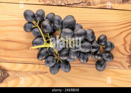 Un rametto di uva nera dolce su un tavolo di legno, macro, vista dall'alto. Foto Stock