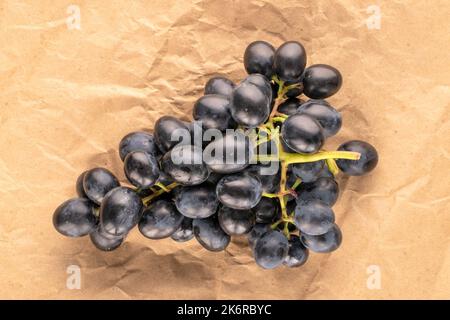 Un rametto di uva nera dolce su carta kraft, macro, vista dall'alto. Foto Stock