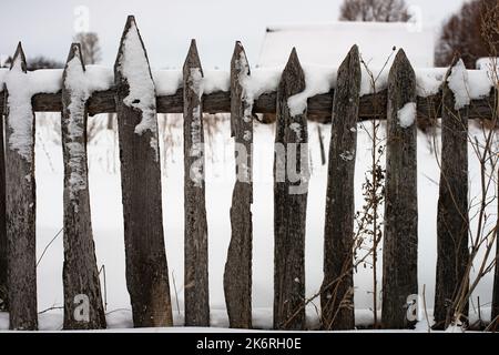 Recinzione in legno con picchetto innevato con fiocchi di neve, sistemazione orizzontale, stagione invernale Foto Stock