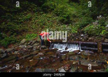 L'escursionista su un lungo sentiero ricarica l'acqua potabile da una sorgente di montagna in un contenitore di vetro. Rifornire di acqua pulita per cucinare e bere mentre ciao Foto Stock