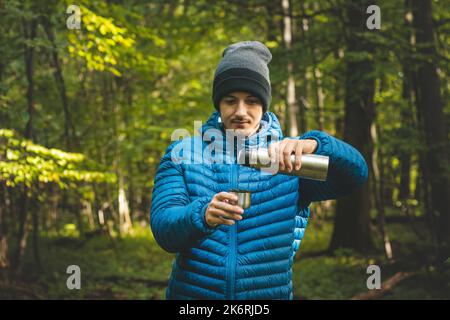 Escursionista su un lungo sentiero prende un riposo e versa il tè caldo da un thermos in una tazza per riscaldare e rifornire vitamine e liquidi. Escursioni in alta montagna. Foto Stock