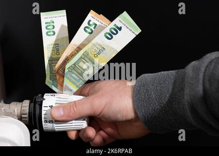 Il termostato di riscaldamento, dotato di banconote in euro, è regolato dalle mani degli uomini Foto Stock