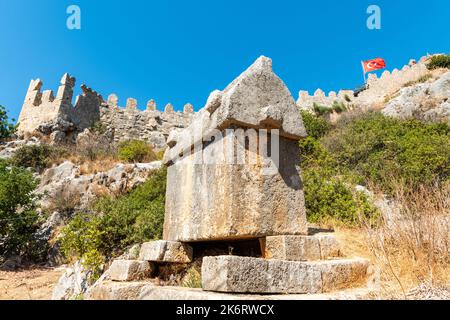 Tomba del sarcofago Liciano vicino al villaggio di Kalekoy nella regione di Kekova nella provincia di Antalya in Turchia. Vista con il castello di Simena in rovina e l'ondeggiante Fla Turca Foto Stock