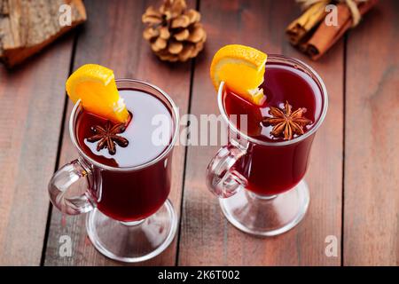 Due bicchieri di VIN brulé con arance e spezie su sfondo ligneo. Bevanda calda autunnale con vino, frutta e spezie. Drink di vino festivo Foto Stock