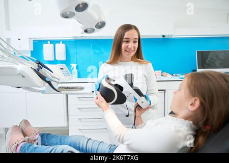 Allegro pedodontista preparare il bambino per l'esame dei denti utilizzando la tecnologia moderna Foto Stock