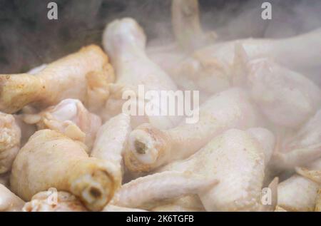 Il cuoco prepara il pollo - cosce e ali in un calderone all'aria aperta. Primo piano. Foto Stock