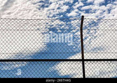 Vista attraverso recinzione a rete metallica, rete metallica su recinzione, cielo nuvoloso, ostacolo immagine simbolo, esclusione, prigionia, immagine di sfondo Foto Stock