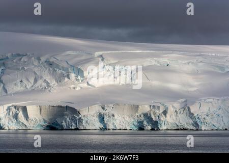 illuminazione mattutina su neve a motivi geometrici e scogliere di ghiaccio della costa. baia di dallmann. penisola antartica. antartide Foto Stock