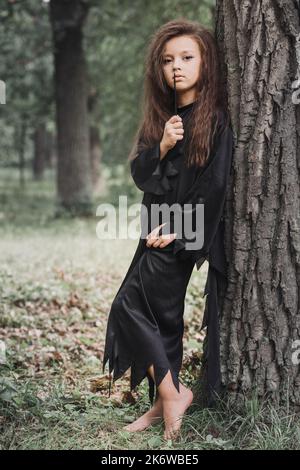 Una piccola strega con una bacchetta magica nella foresta. Concetto di Halloween Foto Stock