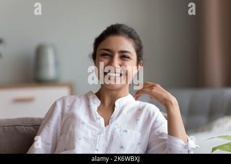 Allegra donna indiana sedersi sul divano sorriso fissando la macchina fotografica Foto Stock