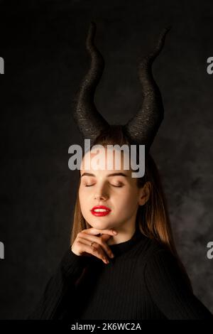 Giovane bella donna con corna lunghe su sfondo nero Foto Stock