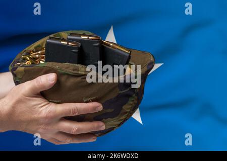 Un casco militare con cartucce e riviste per un fucile nelle mani di un uomo sullo sfondo della bandiera della Somalia. Il concetto di Foto Stock