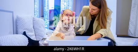 Bambino con disabilità fisica in sala stimolante sensoriale, snoezelen. Bambino che vive con la paralisi cerebrale interagendo con il suo terapeuta durante la terapia Foto Stock