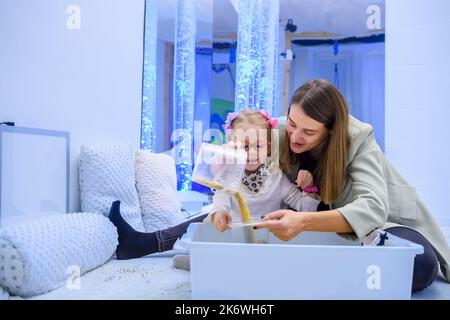 Bambino con disabilità fisica in sala stimolante sensoriale, snoezelen. Bambino che vive con la paralisi cerebrale interagendo con il suo terapeuta durante la terapia Foto Stock