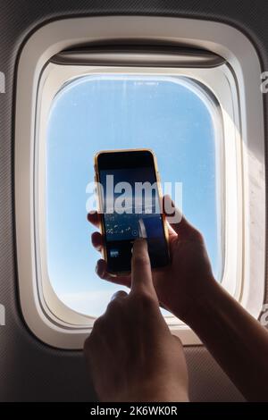 Un passanger sta scattando foto con il suo smartphone in aereo e sta guardando la vista dalla finestra. . Foto di alta qualità Foto Stock