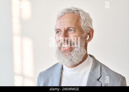 Un vecchio uomo d'affari sorridente che indossa auricolari per ascoltare musica o podcast. Primo piano Foto Stock