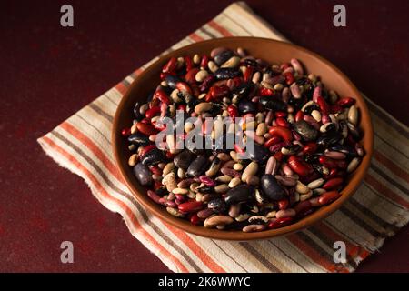 Fagiolini biologici colorati su sfondo bordeaux Foto Stock