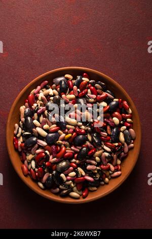 Fagiolini biologici colorati su sfondo bordeaux Foto Stock