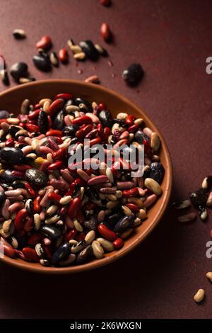 Fagiolini biologici colorati su sfondo bordeaux Foto Stock