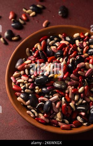 Fagiolini biologici colorati su sfondo bordeaux Foto Stock