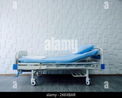 Un letto paziente vuoto regolabile con lenzuola blu e cuscino su sfondo bianco in una stanza d'ospedale. Concetto di assistenza sanitaria, medica e assicurativa. Vari Foto Stock