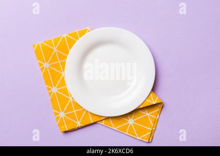 Vista dall'alto su sfondo colorato piatto bianco rotondo vuoto su tovaglia per cibo. Piatto vuoto su tovagliolo con spazio per il vostro disegno. Foto Stock