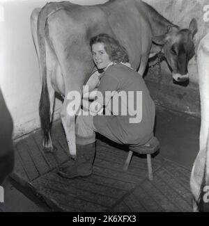 1964, storico, una ragazza adolescente seduta su una piccola mano di sgabello mungendo una mucca, Mayortome Manor, Wendover, Buckinghamshire, Inghilterra, REGNO UNITO. La ragazza è un allievo della Farmhouse School, fondata da Quaker, Isobel Fry intorno al 1900, per i bambini di età compresa tra i 8 e i 18 anni. Tutti gli alunni dovevano alzarsi presto ogni giorno, per prendersi cura degli animali e svolgere le mansioni generali dell'azienda prima della colazione. Si svolgerebbero poi le lezioni tradizionali della scuola. Fry credeva che l'apprendimento di altri argomenti, come la scienza, la natura, la contabilità, è venuto attraverso le attività di lavoro che i bambini hanno intrapreso nella fattoria. Foto Stock