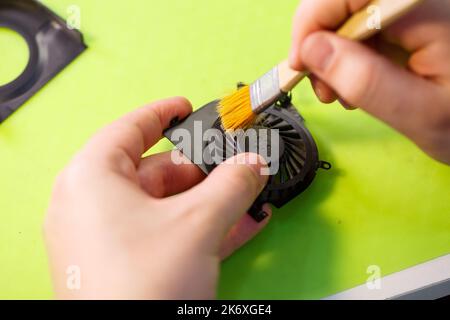 l'uomo pulisce un computer portatile con un attrezzo speciale dalla polvere. Riparazione e manutenzione di computer portatili e PC servizi pubblicitari per la riparazione di componenti elettronici e di elettronica Foto Stock