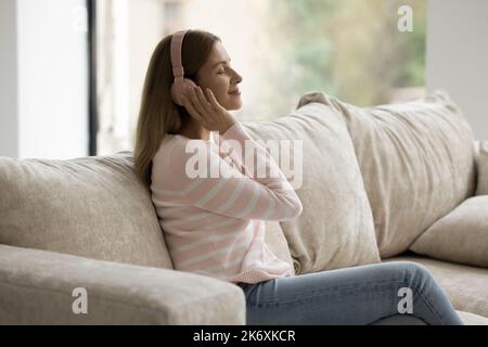 Una donna tranquilla che si rilassa sul divano ascolta la musica attraverso le cuffie Foto Stock