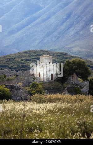 Antica cappella bianca sulle montagne circondata da alberi verdi e cespuglio in Albania Foto Stock