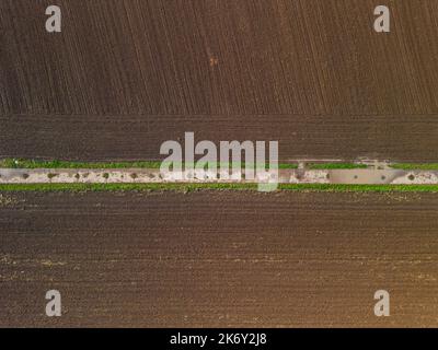 Simmetria e linee tra strada sterrata e campo arato dopo la pioggia Foto Stock