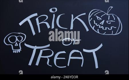 'Trick or treat' scritto con gesso su una lavagna con un jack-o-lanterna sorridente e un sole Foto Stock