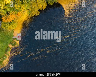 coppia posata sul molo al lago coperto di foglie autunnali Foto Stock