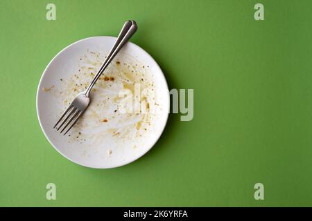 Piatto in ceramica bianca con avanzi di cibo, pasta, olio d'oliva, salsa e forchetta su fondo verde. Immagine creativa con spazio per il testo Foto Stock