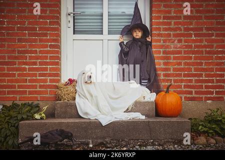 Adorabile bambino con cane sul portico vestito in costumi di Halloween Foto Stock