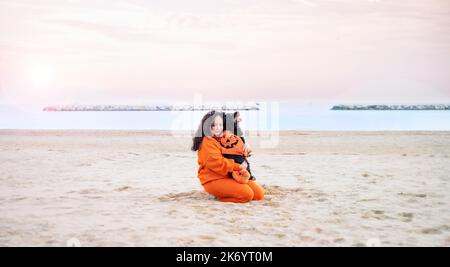 Halloween cane vestito come una zucca sulla spiaggia. Black Cocker Spaniel in abiti festosi gioca con il suo proprietario. Autunno terrapieno e una bella passeggiata. Riprese in 4K di alta qualità Foto Stock