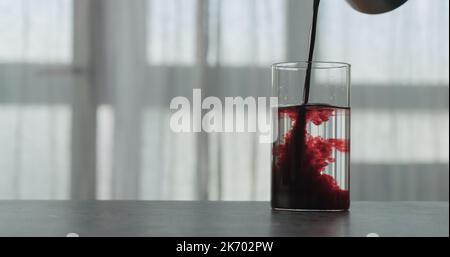 versare il succo di mirtillo in acqua in vetro su un piano di cemento con finestra sullo sfondo, foto ampia Foto Stock