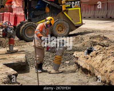 Medellin, Antioquia, Colombia - Giugno 2 2022: Uomo colombiano che lavora in costruzione con un Rammer di manomissione elettrica che indossa una uniforme arancione di sicurezza AN Foto Stock