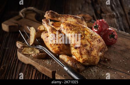 Dall'alto gustoso pollo intero arrosto con pomodori e patate servito sul tritare legname durante il pranzo Foto Stock
