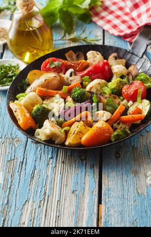 Da sopra la padella con deliziose verdure fritte poste sul tavolo di legno stagionato vicino alle erbe fresche e bottiglia di olio durante il pranzo Foto Stock