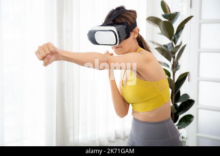 Giovane donna caucasica che indossa il visore vr mentre si allena e si esercita insieme nel salotto di casa, futuristica e innovativa del metaverse della realtà virtuale, f Foto Stock