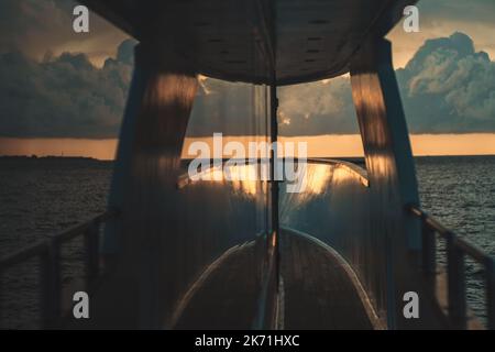 Vista astratta con una profondità di campo poco profonda e una messa a fuoco selettiva su una parte di un pavimento in legno di uno yacht con uno splendido tramonto sull'oceano simmetricamente re Foto Stock