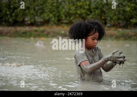 Ragazza felice afroamericana che gioca in pozza di fango bagnato durante piovendo nella stagione piovosa. Foto Stock