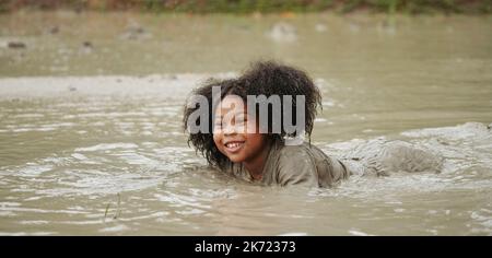 Ragazza felice afroamericana che gioca in pozza di fango bagnato durante piovendo nella stagione piovosa. Foto Stock