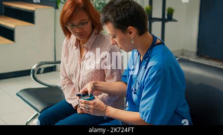 Infermiere che misura il livello di insulina e glucosio con glucometro, facendo un esame cehckup con paziente asiatico diabetico. Utilizzo di insturment per controllare il campione di sangue, diabete consultazione. Foto Stock