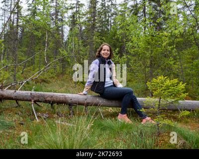 donna seduta su un albero caduto in una foresta verde Foto Stock