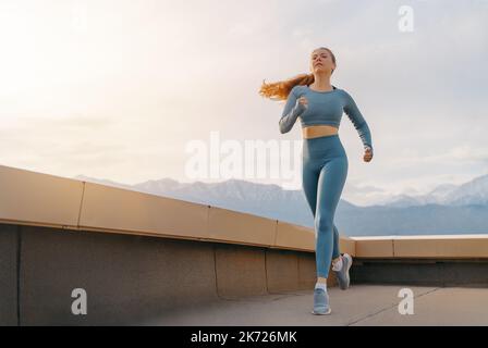 Donna atletica è in esecuzione sul tetto del parcheggio, garage su sfondo tramonto. Foto Stock