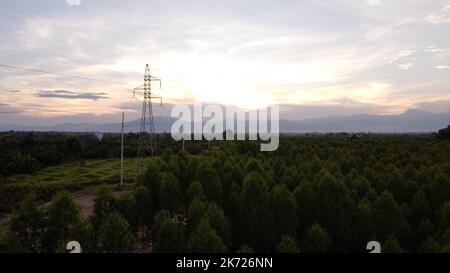 Vista aerea di tralicci e fili ad alta tensione nel cielo al tramonto in campagna. Riprese drone di poli elettrici e fili al crepuscolo. Foto Stock