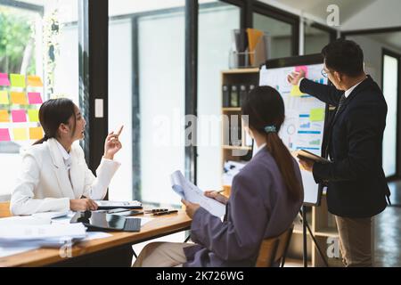 Consulente aziendale che spiega la strategia del business plan su lavagna a fogli mobili a colleghi, allenatore maschile o consigliere che presenta al briefing, riferisce su Foto Stock